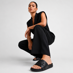 Person wearing a black outfit with sandals on a plain background