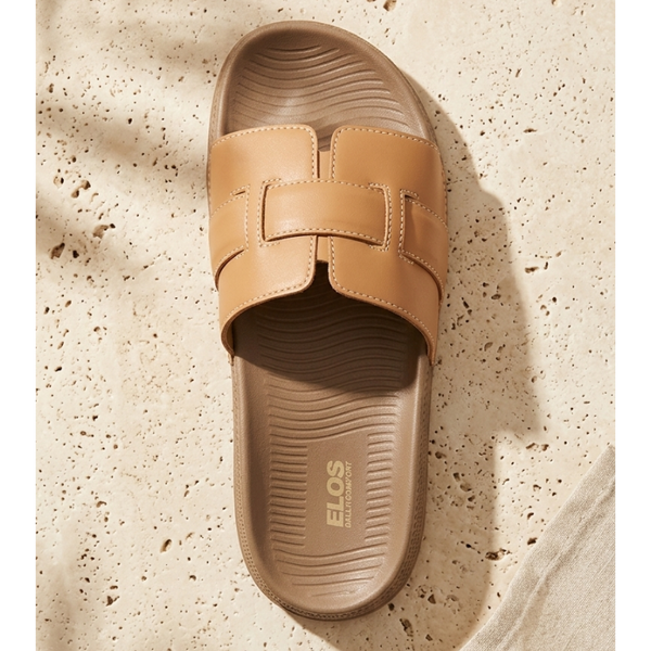 Tan slide sandal with 'Elos' branding on a textured beige surface